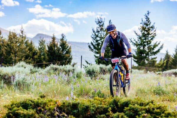 Butte photography of Butte 100 racer smiling while riding bike with wildflowers beside trail