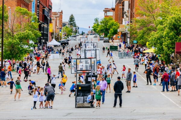 Wide view of Uptown Hoops, showing multiple street basketball courts and crowds gathered in historic Uptown Butte, Montana.