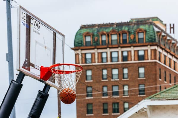 Basketball dropping through an outdoor hoop during Uptown Hoops, with the historic Hotel Finlen visible in Uptown Butte, Montana.