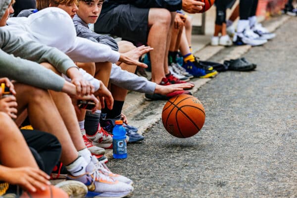Youth basketball players sitting along the curb during a community street basketball event in Butte, Montana.
