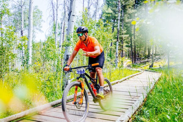 Butte photography of Butte 100 racer giving peace sign to camera while riding bike