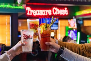 Group of 3 holding up cocktails and cheersing in front of bar signage