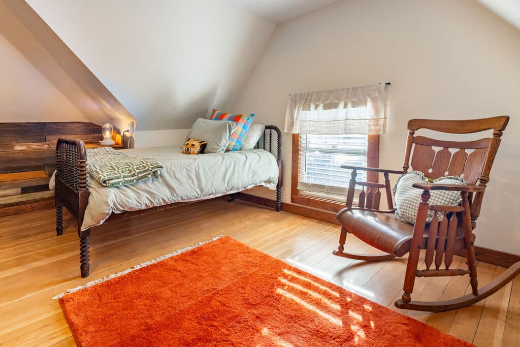 Cozy Montana Airbnb kids bedroom with natural light, vintage rocking chair, heart pillow, and warm wood floors photographed with realistic vacation rental styling.